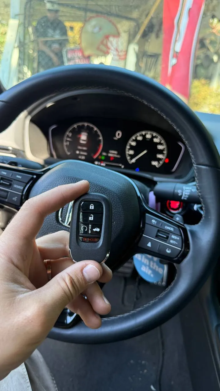 Honda smart key held in front of the steering wheel and dashboard of a Honda