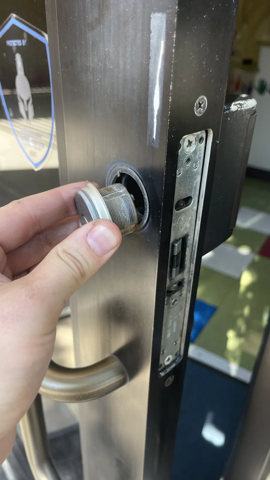 Hand removing a mortise lock cylinder from an aluminum storefront door