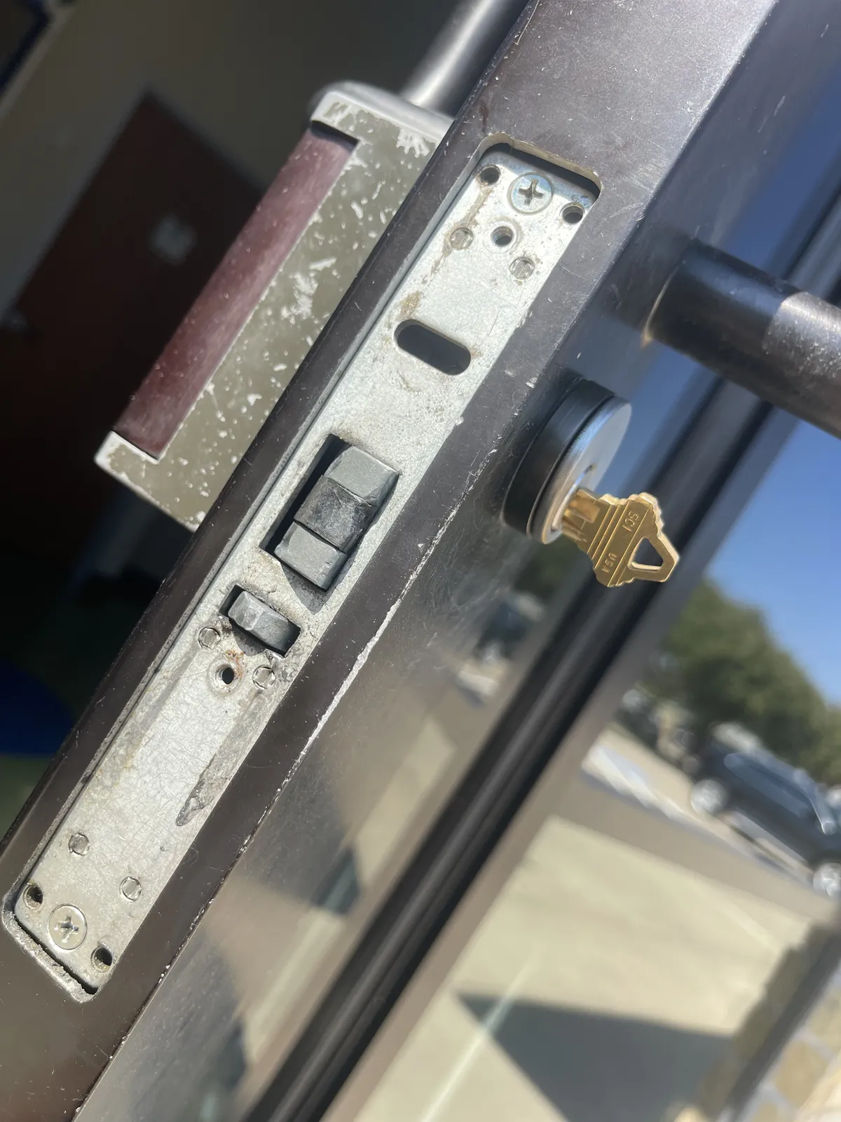 Mortise lock body exposed in the edge of an aluminum storefront door, key in the cylinder