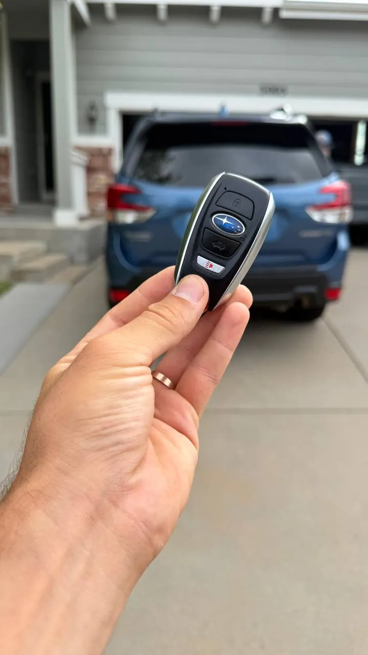 Subaru smart key held in front of a blue Subaru Forester in a driveway